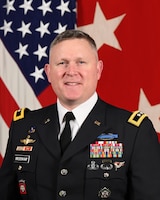 Portrait of Major General Trevor Bredenkamp dressing in Army service dress uniform with the US flag and red 2-star general flag in the background.
