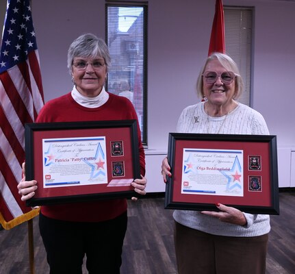 two woman stand together holding framed awards