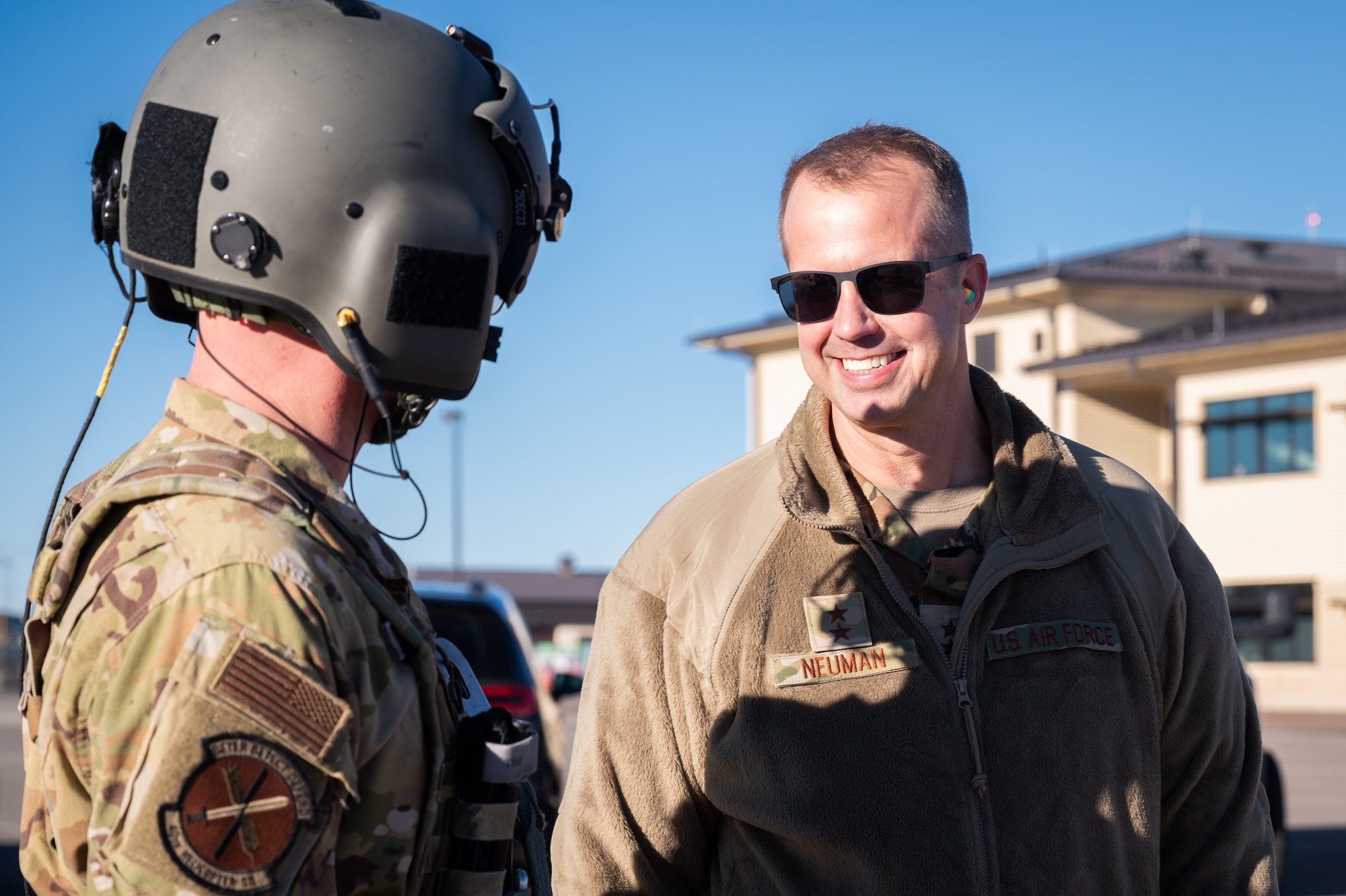 A man in military uniform and sunglasses smiles to greet a military pilot in front of him.