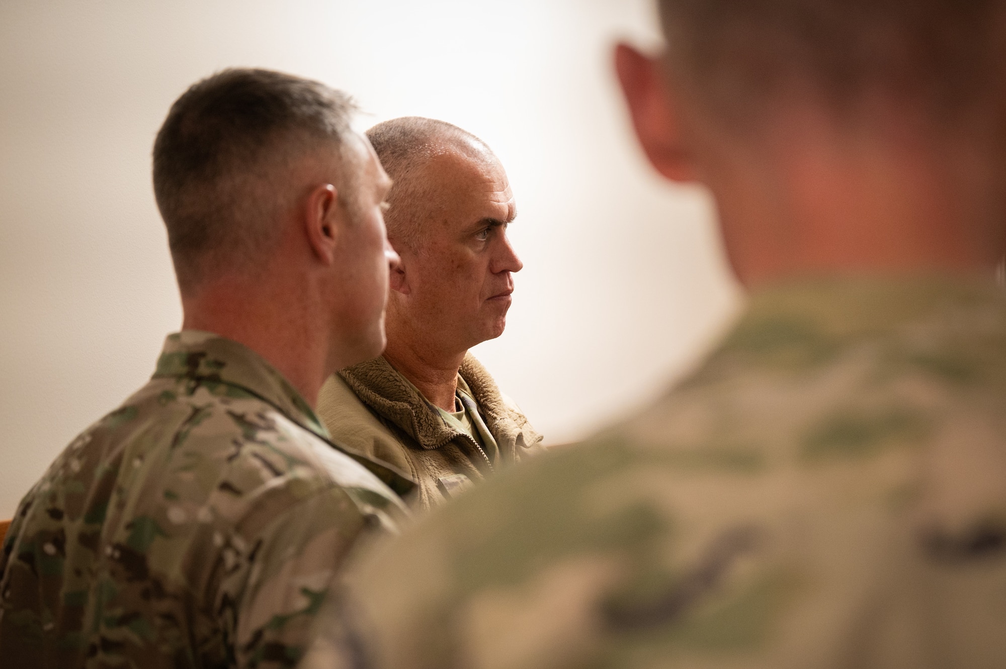 The side profile of a man in military uniform is in focus between two others as they talk.