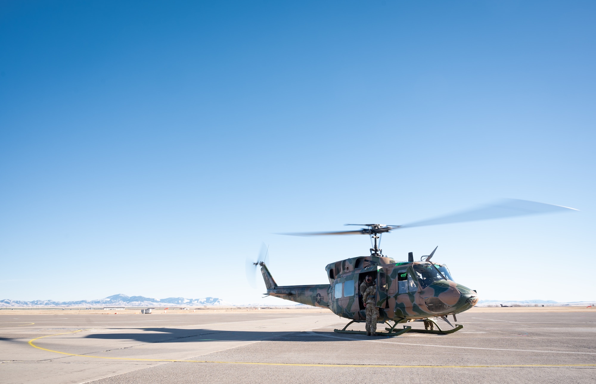 A helicopter sits on a flightline with mountain range faintly visible in the background.