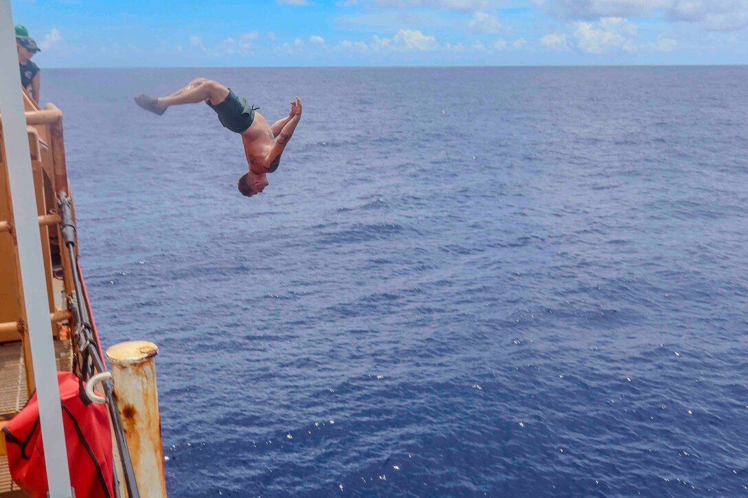 A Coast Guardsman backflips from a ship into a body of water.