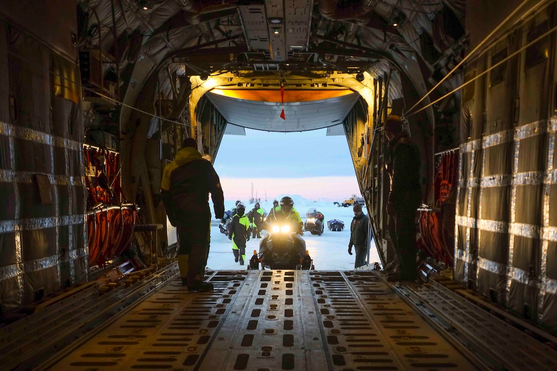 Marines load snow machines into a parked aircraft.