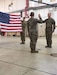 Two Soldiers face each other during a swear in, while a third Soldiers stands behind them holding the American flag