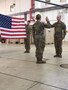 Two Soldiers face each other during a swear in, while a third Soldiers stands behind them holding the American flag