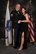 Soldier in dress uniform stands with a women in a black formal dress in front of a recruiting flag and the American flag