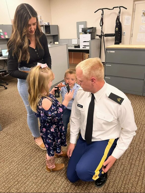 Soldier in uniform getting patches put on by his son and daughter. The Soldier's wife is standing behind the kids.