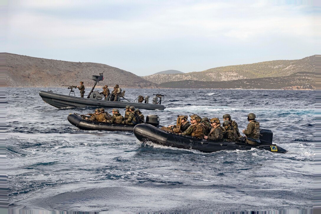 Three boats sail in formation carrying U.S. and Greek marines with mountains in the background.