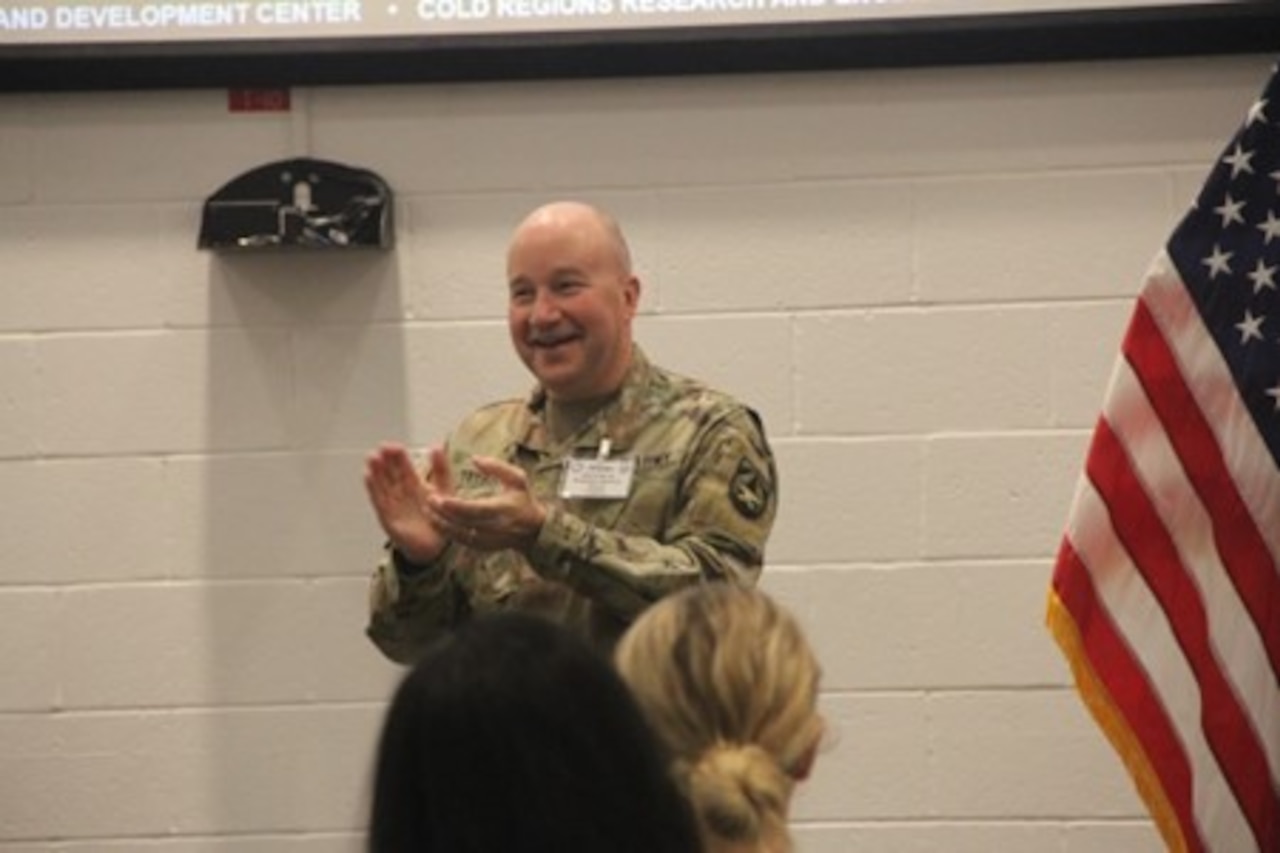 A person claps while speaking in front of an audience.