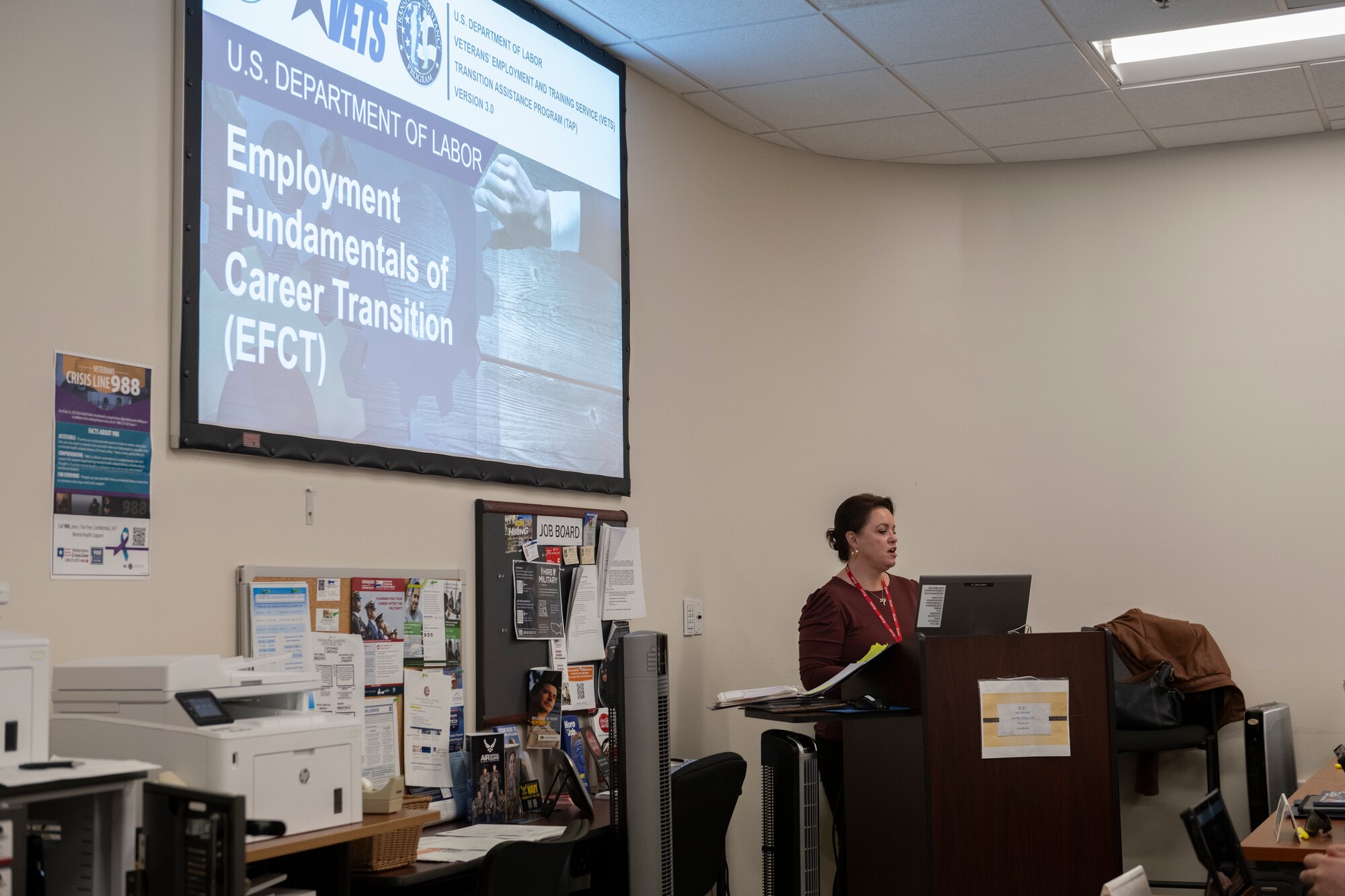 A photo of a projector and a teacher standing next to it at a podium.