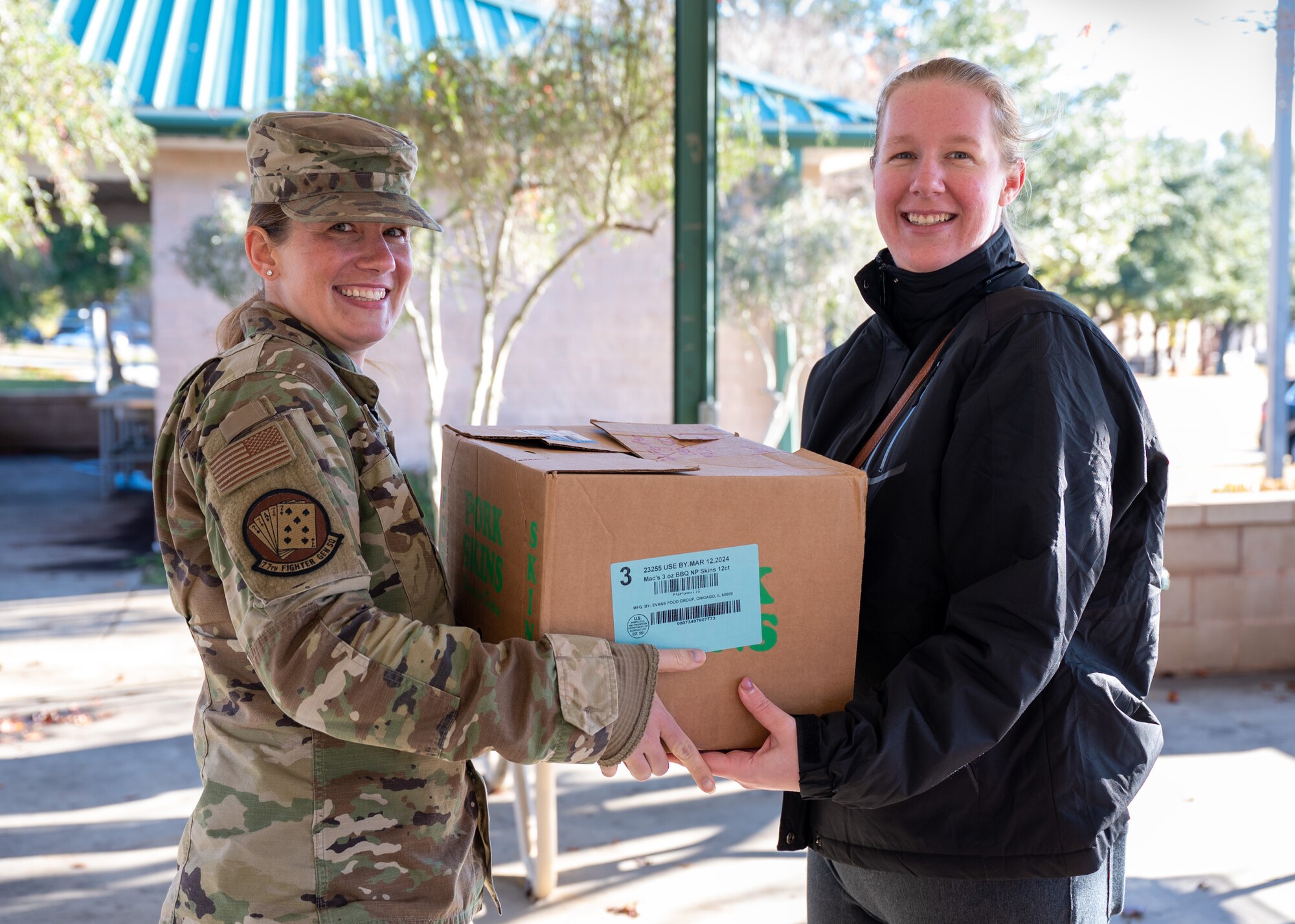 Two women hold a box between them and pose for a photo.