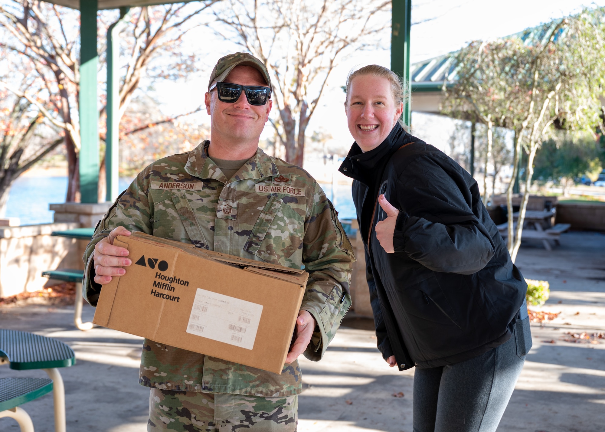 A man holds a box of donated goodies as a woman gives a thumbs up.