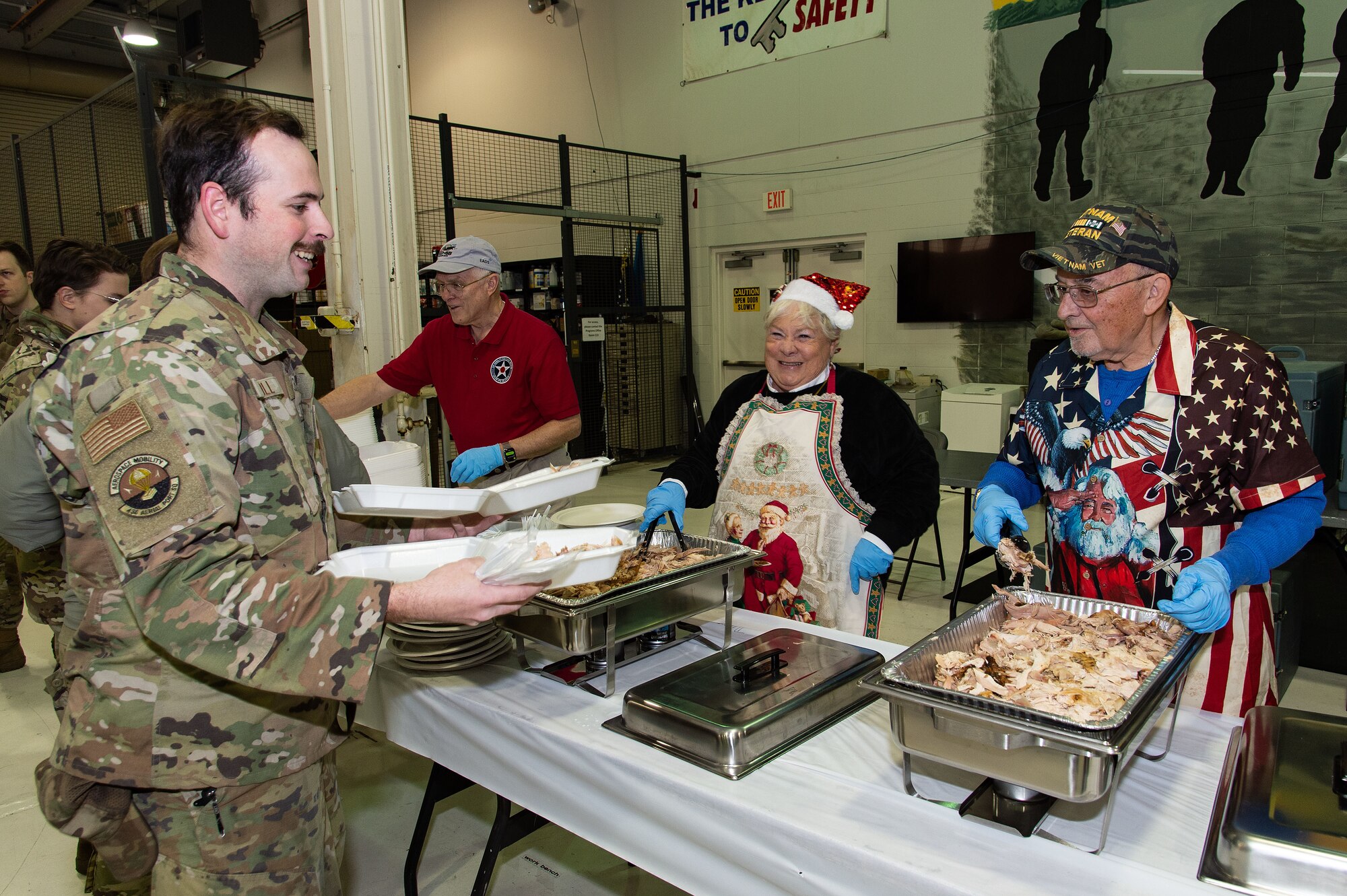 U.S. Air Force Senior Airman Braden Toll, left, 436th Aerial Port Squadron cargo processor, receives a serving of turkey from Patti, center, and Ron Papineau, right, as he goes through the Operation Feed the Troops food line at Dover Air Force Base, Delaware, Dec. 13, 2023. The Papineau’s are volunteers at the Air Mobility Command Museum and have been OFTT volunteers the past three years. (U.S. Air Force photo by Roland Balik)