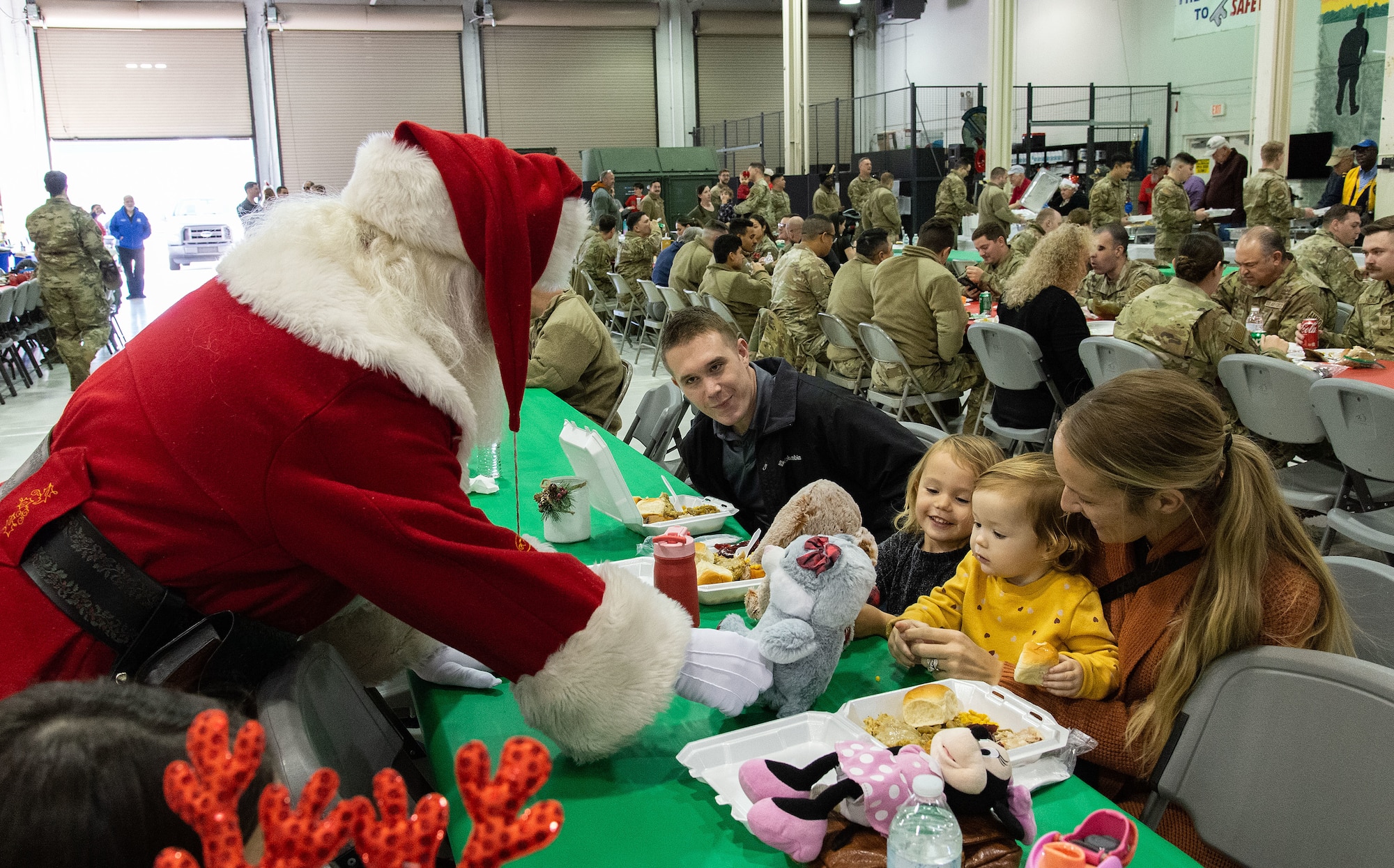 Greg ‘Santa’ Miller hands a stuffed animal to Myla MacIntyre, as her older sister Ava, watches while attending the Operation Feed the Troops meal at Dover Air Force Base, Delaware, Dec. 13, 2023. The two are the daughters of U.S. Army Sgt. 1st Class Lawrence MacIntyre, center, University of Delaware Army ROTC, Newark, Delaware, and his wife Jalena, right, who brought their children to the day meal and to meet Santa. (U.S. Air Force photo by Roland Balik)