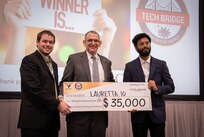 Mr. Peter C. Reddy, middle, executive director of Naval Information Warfare Center (NIWC) Atlantic, and Dr. Luke Overbey, left, NIWC Atlantic’s senior scientific technical manager for autonomy, present a $35,000 check to Lauretta.io on Dec. 7 for winning first place in the Multilateral Autonomy Prize Challenge at the 2023 Eastern Defense Summit.
