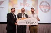 Mr. Peter C. Reddy, middle, executive director of Naval Information Warfare Center (NIWC) Atlantic, and Dr. Luke Overbey, left, NIWC Atlantic’s senior scientific technical manager for autonomy, present a $15,000 check to Quartus on Dec. 7 for taking second place in the Multilateral Autonomy Prize Challenge at the 2023 Eastern Defense Summit.