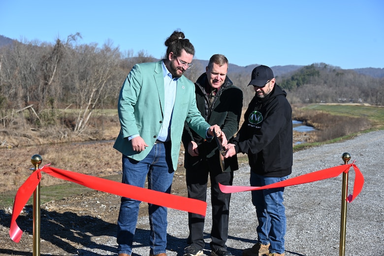 Three men stand cutting ribbon with oversized scissors.