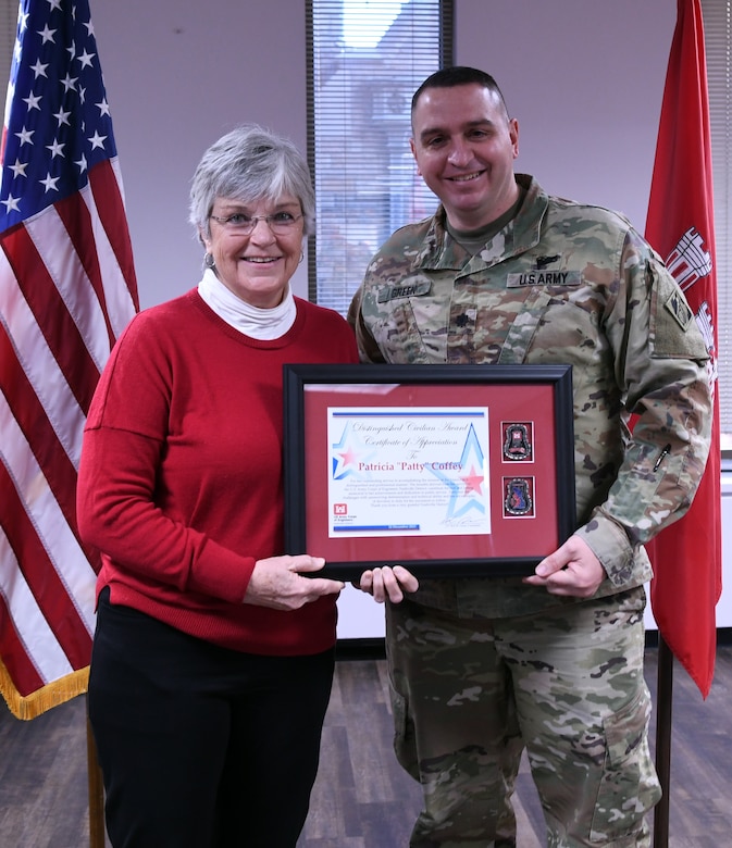 man stands with woman holding framed award together