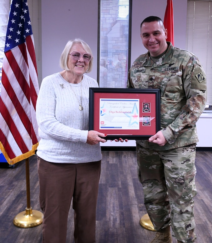 man stands with woman holding framed award together