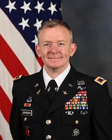 U.S. Army Col. Mark Johnson poses for his official portrait in the Army portrait studio at the Pentagon in Arlington, Va., June 16, 2023. he is dressed in his Army dark blue dress uniform and behind him is the US Flag.  (U.S. Army photo by Leonard Fitzgerald)