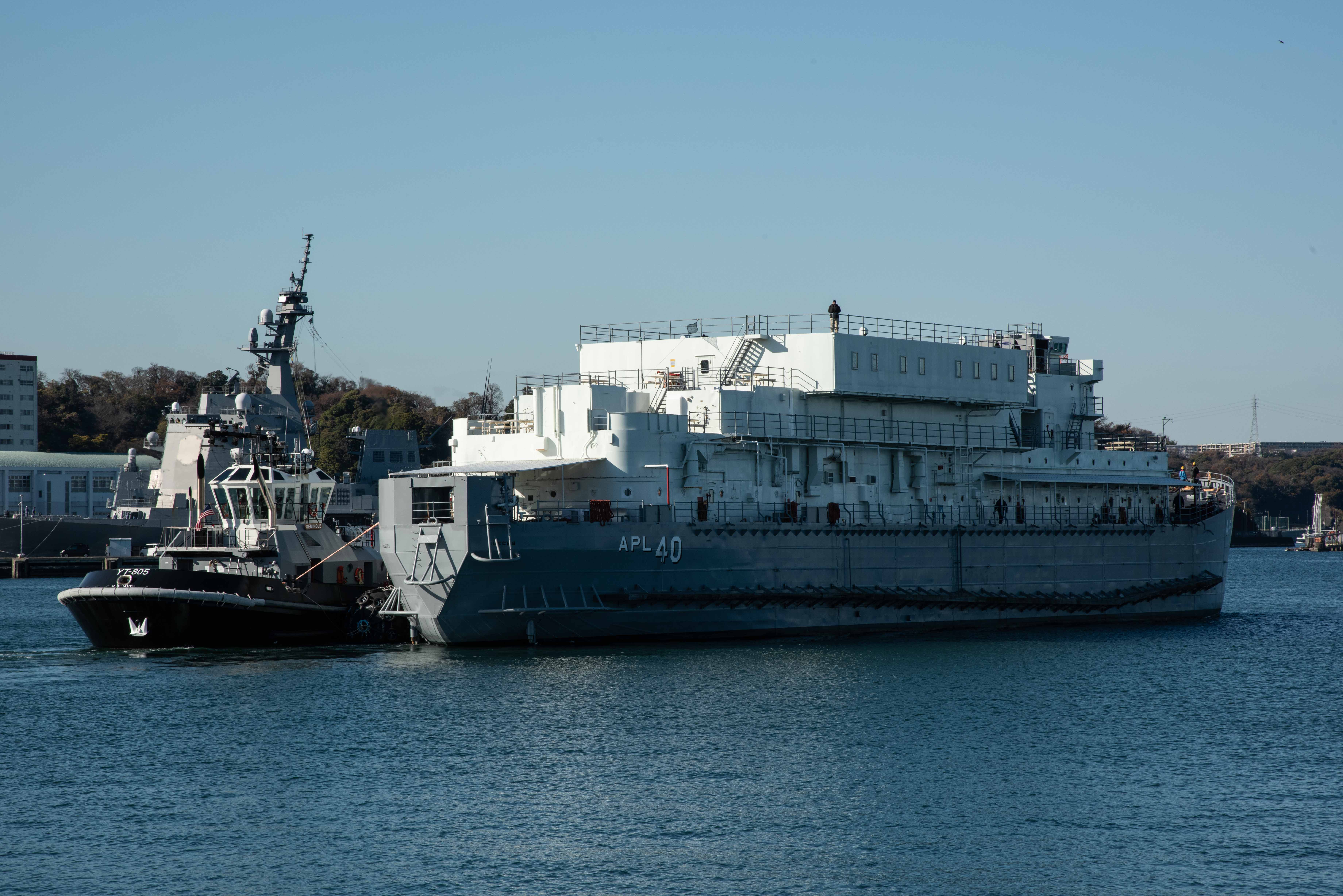 Military berthing barge is being guided by tugboats away from the pier.