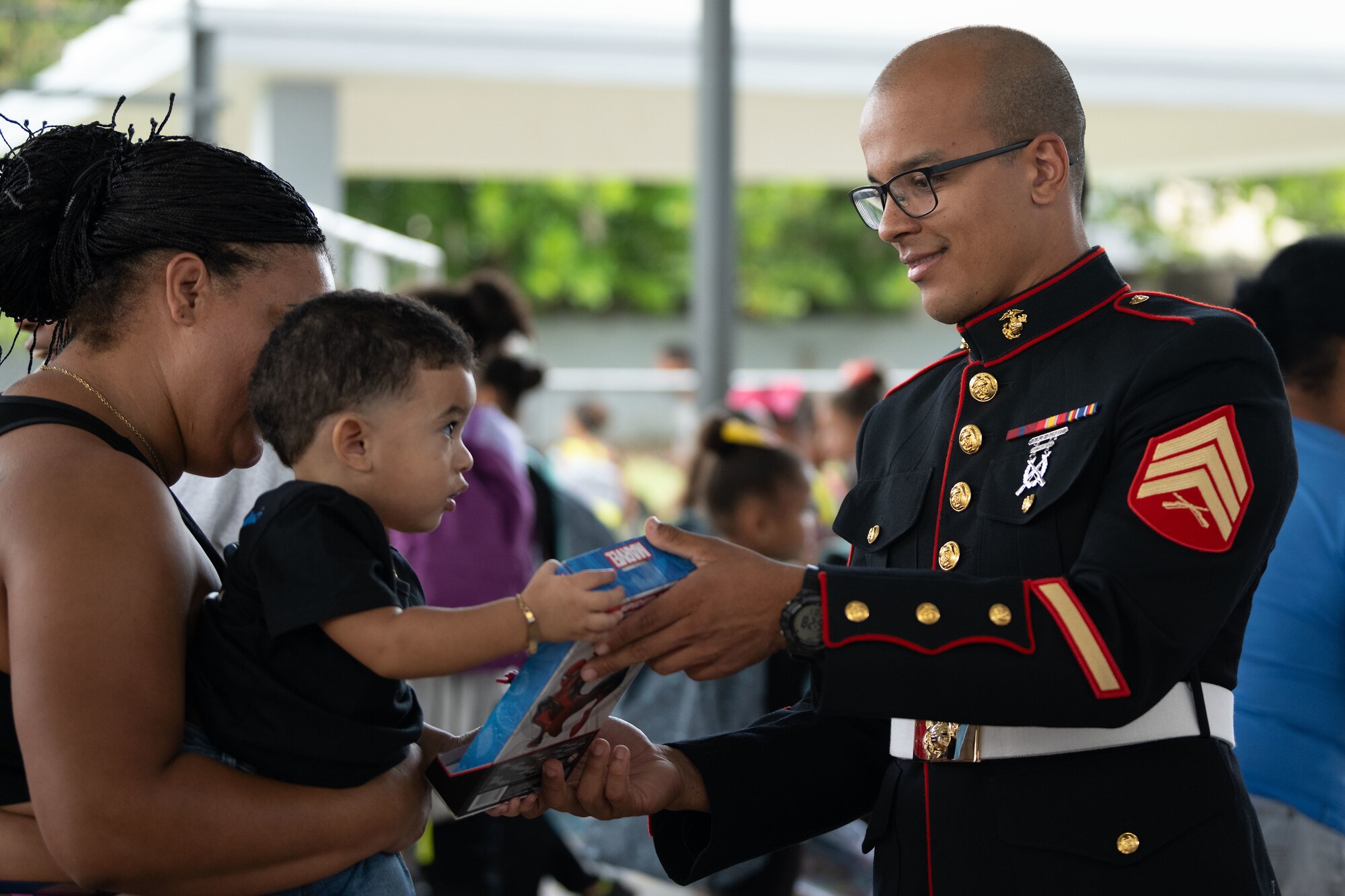 U.S. Marine Corps Sgt. Yadiel Burgos Benitez, a Toys for Tots coordinator, both assigned to Det. 1 Landing Support Company, Combat Logistics Regiment 45, 4th Marine Logistics Group, deliver toys to a child and his mother during a toy distribution at Dr. Julio Henna Elementary School, San Juan, Puerto Rico, Dec. 14, 2023. The event was part of the campaign with Toys for Tots, where Puerto Rico Air National Guard members partnered with Marines to distribute more than 200 toys to children at a local school. (U.S. Air National Guard photo by Airman 1st Class Gisselle Toro-Caraballo)