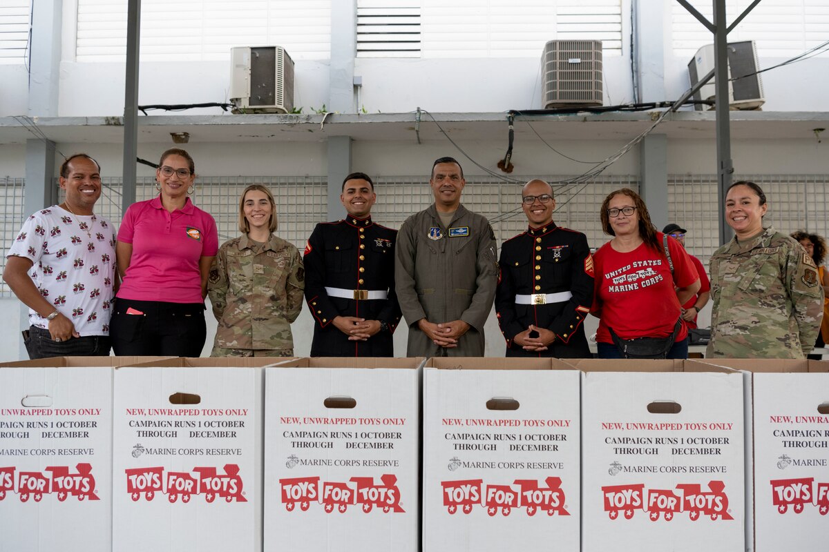 U.S. Airmen with the 156th Wing, Puerto Rico Air National Guard, U.S. Marines assigned to Det. 1 Landing Support Company, Combat Logistics Regiment 45, 4th Marine Logistics Group, and faculty members pose for a photo during a toy distribution at Dr. Julio Henna Elementary School, San Juan, Puerto Rico, Dec. 14, 2023. The event was part of the campaign with Toys for Tots, where PRANG members partnered with Marines to distribute more than 200 toys to children at a local school. (U.S. Air National Guard photo by 2nd Lt. Eliezer Soto)