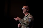 A person in a uniform and eyeglasses is shown gesturing during a speech.