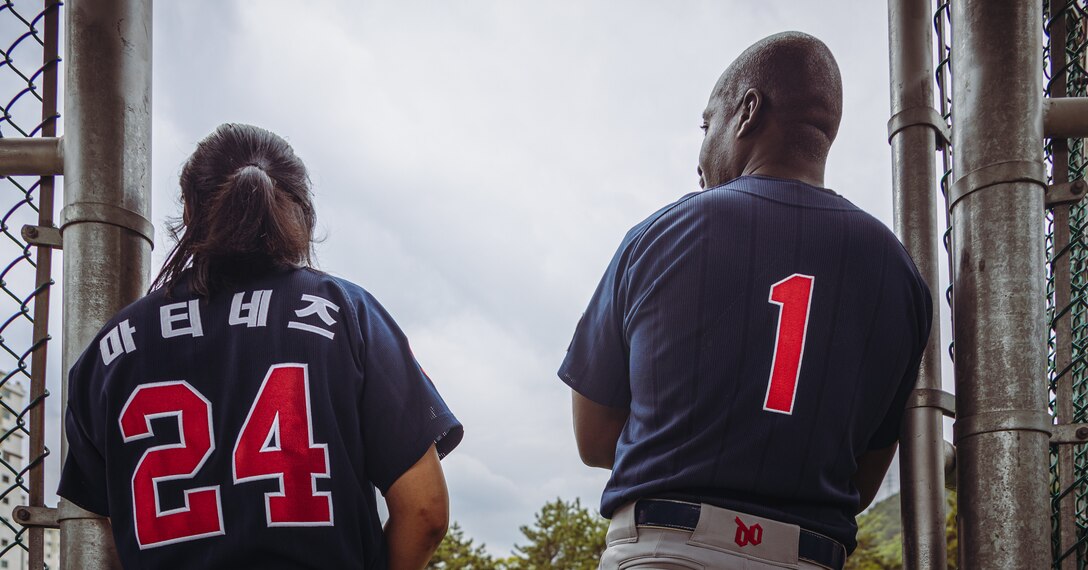 U.S. Marine Corps Cpl. Alexandria Martinez, left, a patrolman with Security Forces, Camp Mujuk, and Staff Sgt. Danny Thomas, right, the training chief with S-3, Camp Mujuk, stand by  during a softball game on Commander Fleet Activities Chinhae, South Korea, April 15, 2023. Each team that participated in the game played under a respective league, but in the Pohong region of South Korea, the Camp Mujuk team was the only team representing a non-Korean entity. Although it was acknowledged as a team affiliated with the Marine Corps, members were not limited to any specific branch of service, and the team consisted of a diverse group of individuals, including sailors and civilians. (U.S. Marine Corps photo by Lance Cpl. Jonathan Beauchamp)