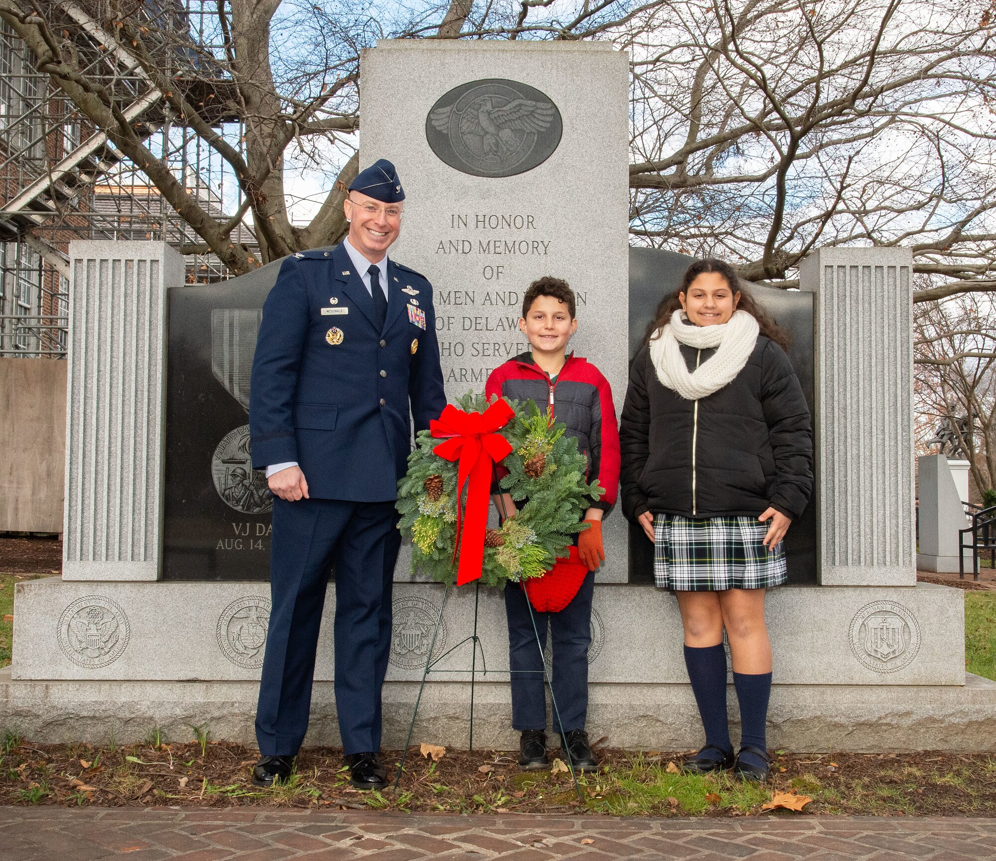 U.S. Air Force Col. Chris McDonald, left, 436th Airlift Wing commander, takes a photo with Holy Cross Elementary School fourth grade students William May, center, and Gaia Zappulo, right, after the Wreaths Across America ceremony held at Legislative Hall, Dover, Delaware, Dec. 11, 2023. McDonald, May, and Zappulo placed a ceremonial wreath at the World War II Memorial after the ceremony. National WAA Day is Dec. 16. (U.S. Air Force photo by Roland Balik)