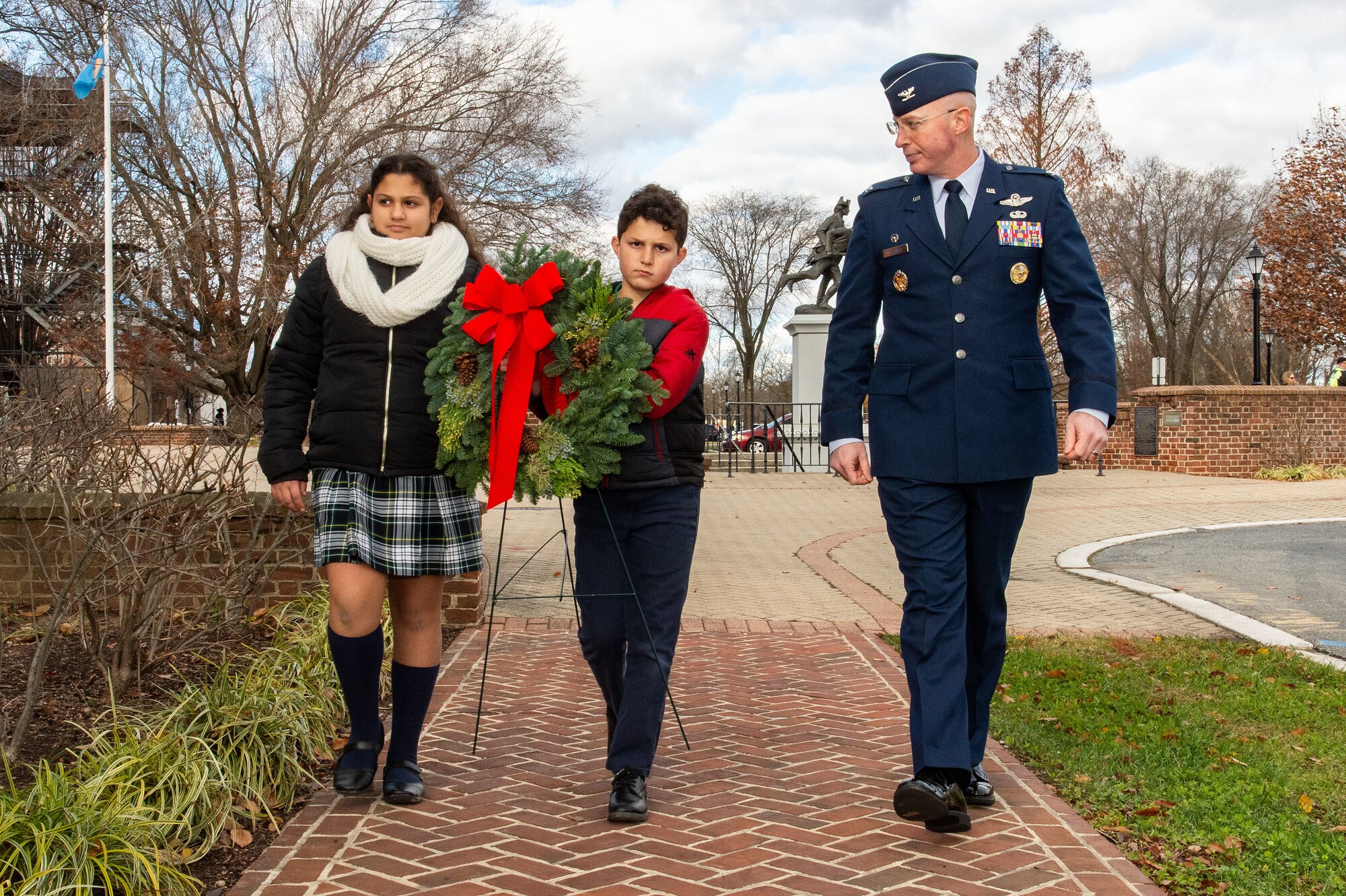 U.S. Air Force Col. Chris McDonald, right, 436th Airlift Wing commander, walks with Holy Cross Elementary School fourth grade students Gaia Zappulo, left, and William May, center, after the Wreaths Across America ceremony held at Legislative Hall, Dover, Delaware, Dec. 11, 2023. McDonald, Zappulo, and May placed a ceremonial wreath at the World War II Memorial after the event. National WAA Day is Dec. 16. (U.S. Air Force photo by Roland Balik)