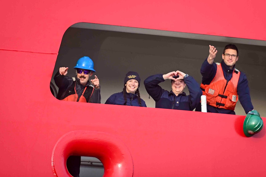 Four Coast Guardsmen make gestures through an opening on a ship.