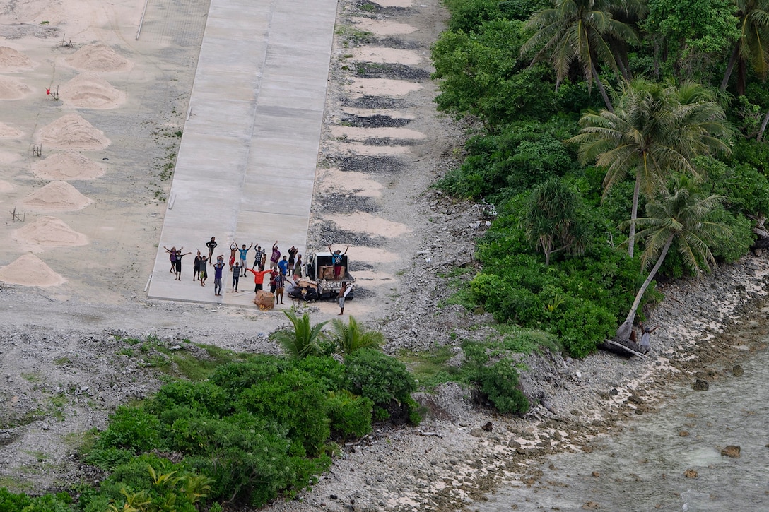 Residents wave and cheer at a plane above them from a makeshift runway.