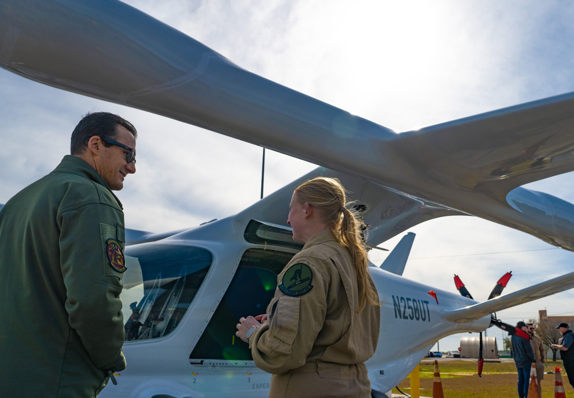 Two military members talk next to an electric aircraft.