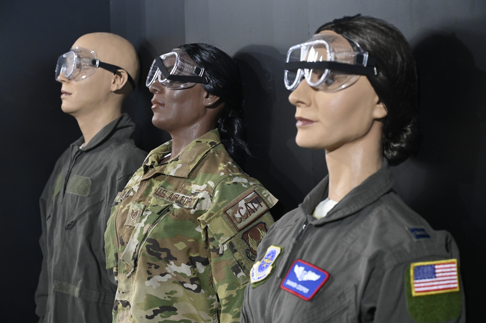 Image of 3 manequins from the critical care component of the humanitarian exhibit. The manequins are all dressed in a service uniform, wearing safety goggles and portray flight medical staff who treat patients in transport.