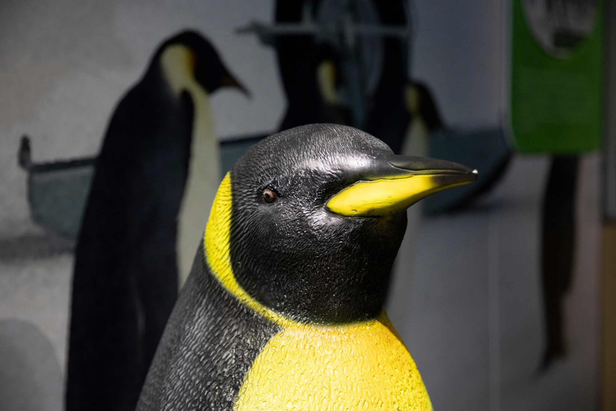 Image of a fabricated emperor penguin located in the Goodwill missions portion of the humanitarian exhibit. The penguin has a black head and back, and a yellow beak with a wrap of yellow color around it's neck and down it's chest.