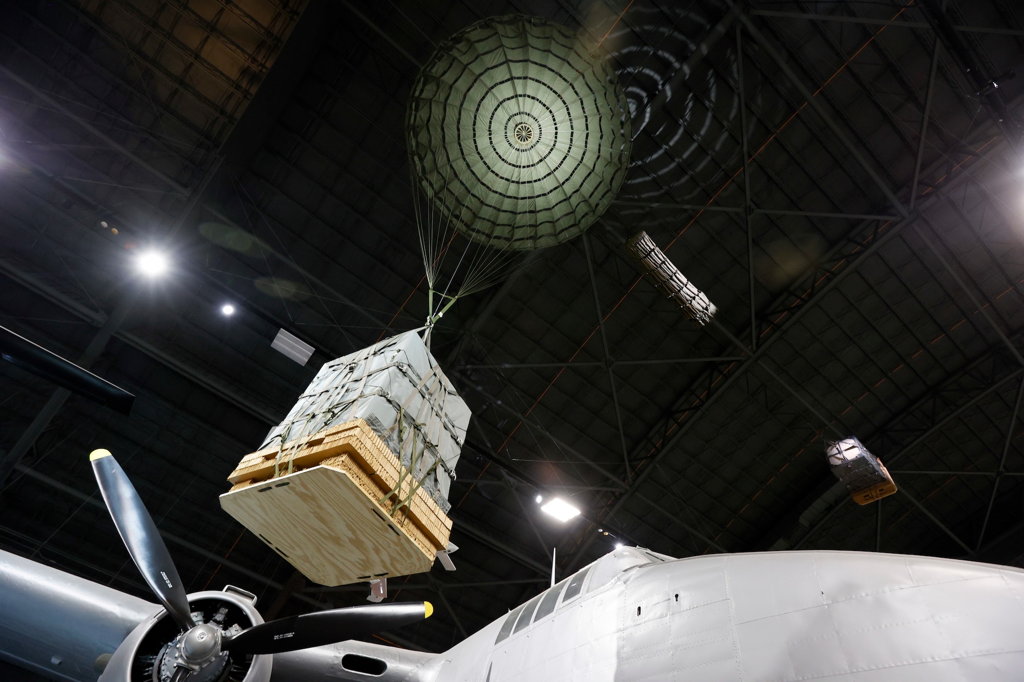 Image of a pallet being suspended from the ceiling of the museum's 4th hangar with a parachute open at the top to replicate the aerial delivery mission of the Air Force