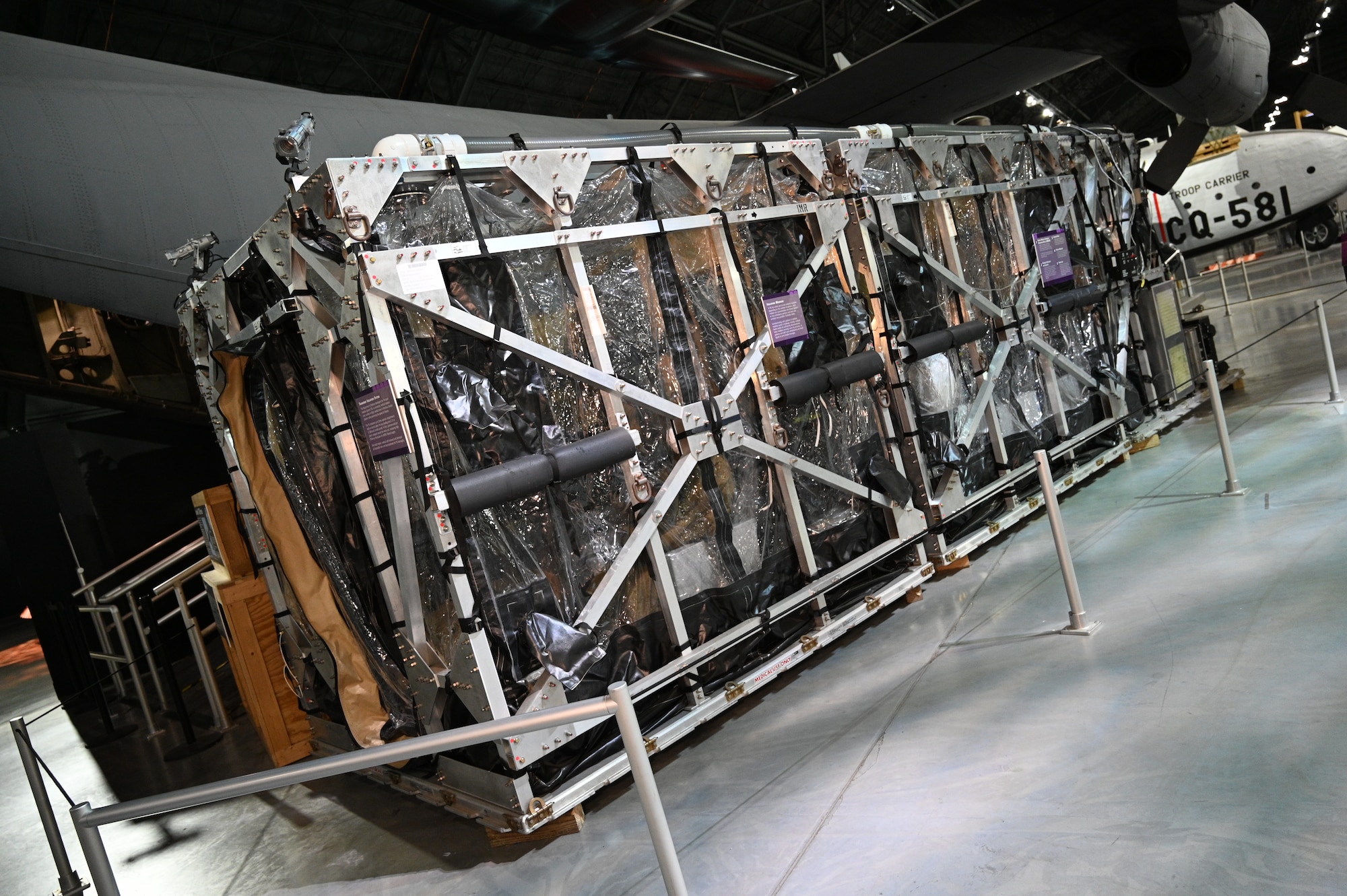 Exterior image of the Transport Isolation System. It is a long rectangular box with a steel frame covered in clear plastic.