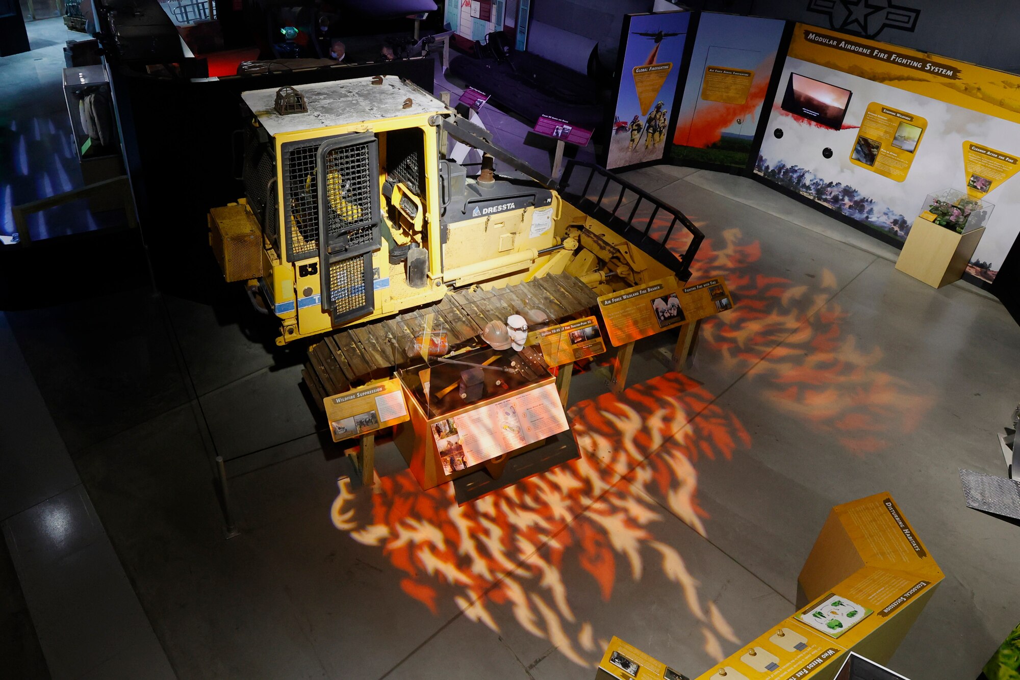 Image of the bulldozer used by firefighters, which is placed in the Global Firefighting mission portion of the Humanitarian exhibit. In front of the bulldozer, lights on shining on the floor to replicate flames.