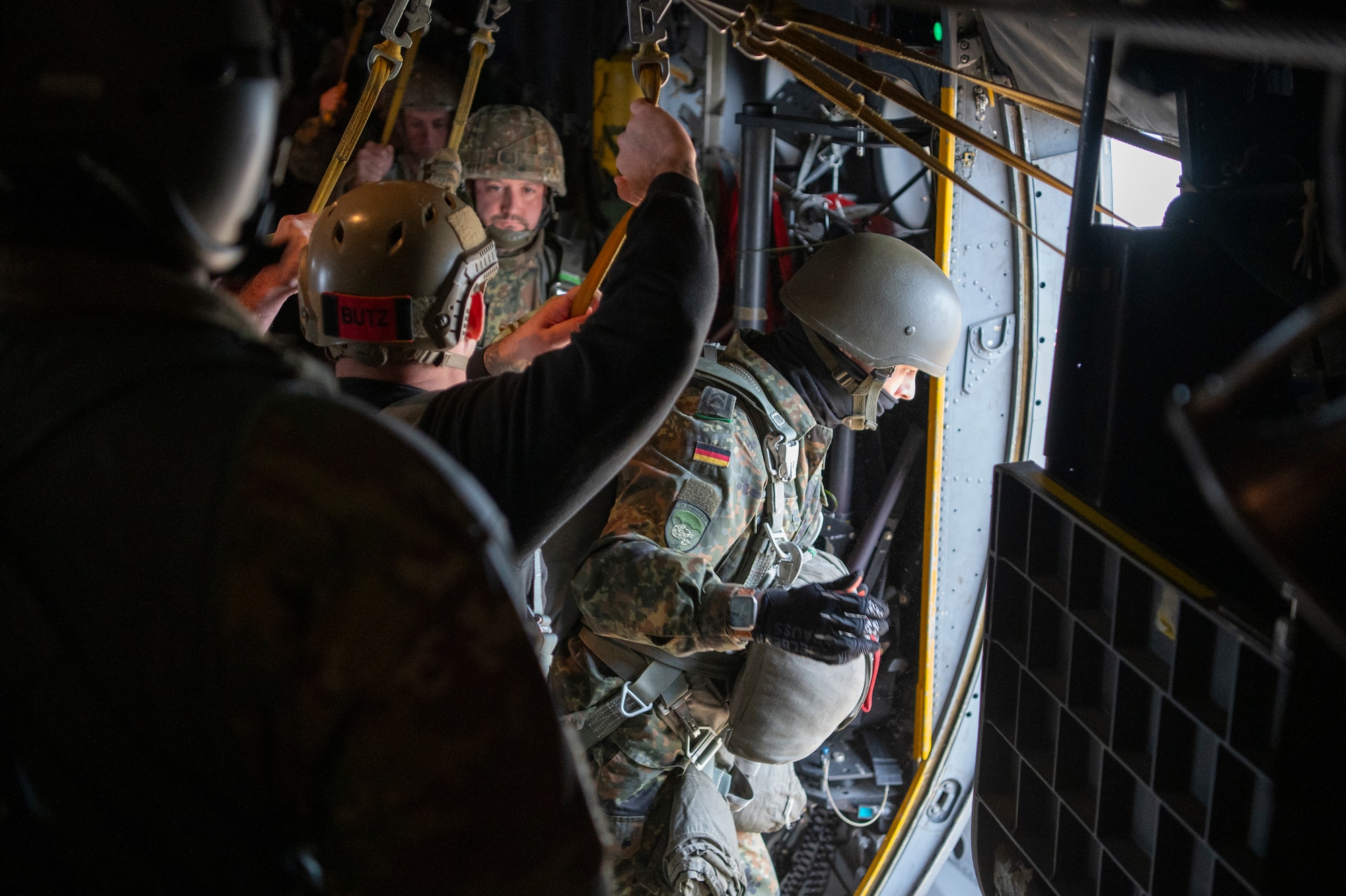 a person in a military uniform crouches beside an open aircraft door preparing to parachute out of it