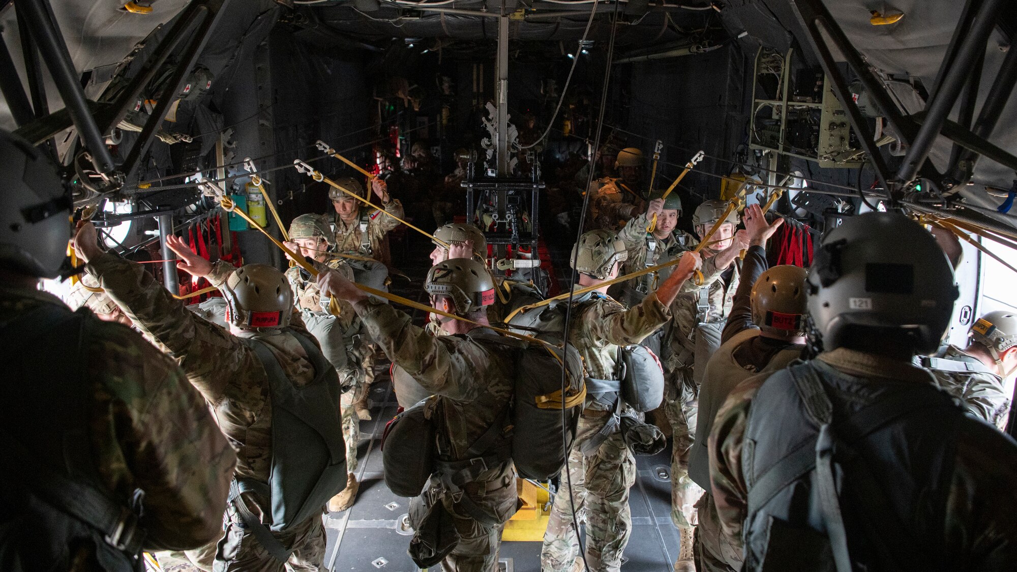 people in military uniforms stand inside an aircraft waiting to parachute