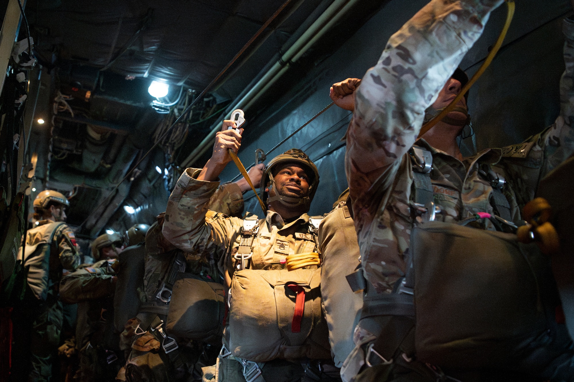 people in military uniforms stand inside an aircraft waiting to parachute