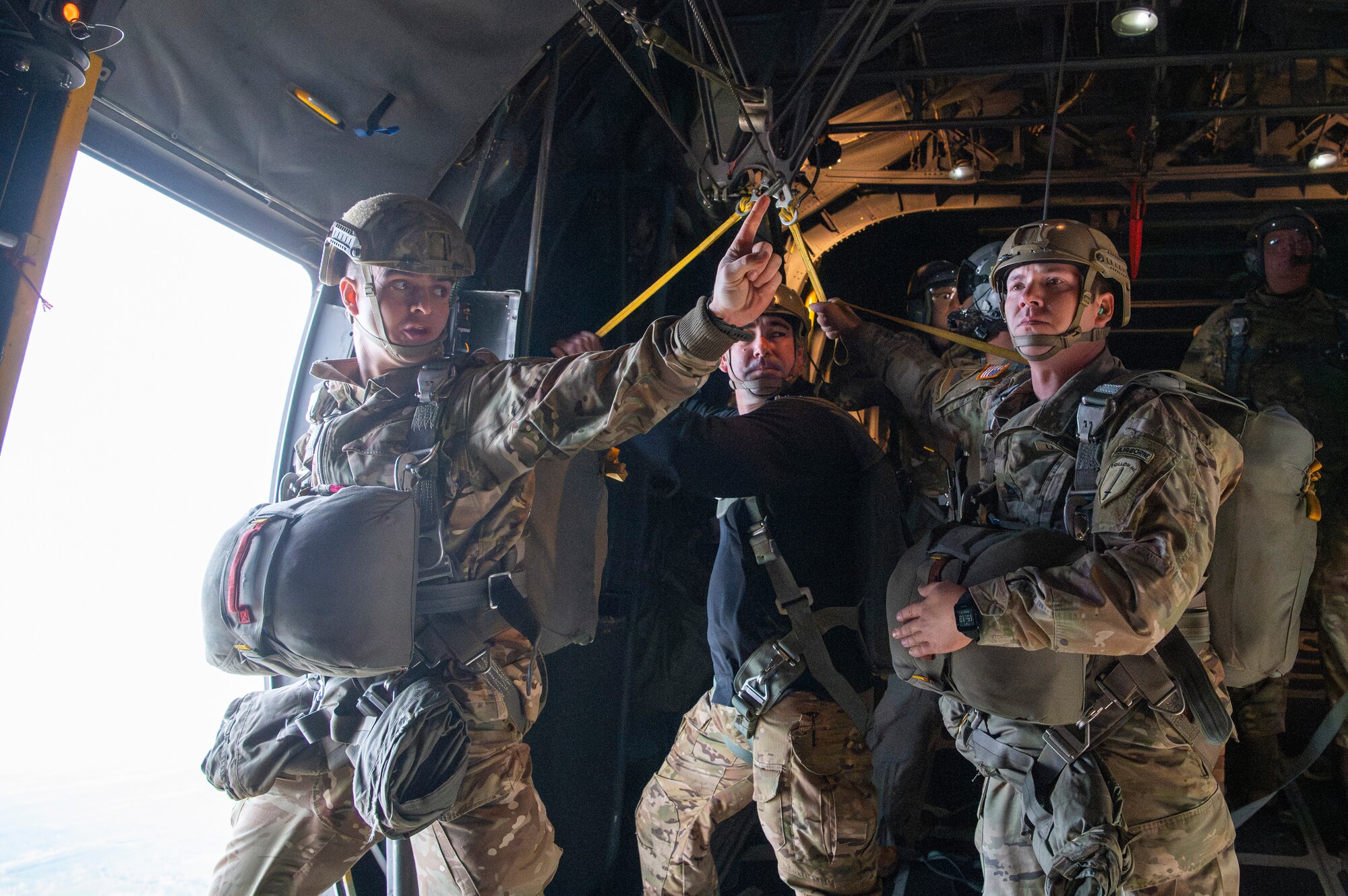 three people in military uniforms stand beside an open aircraft door preparing to parachute