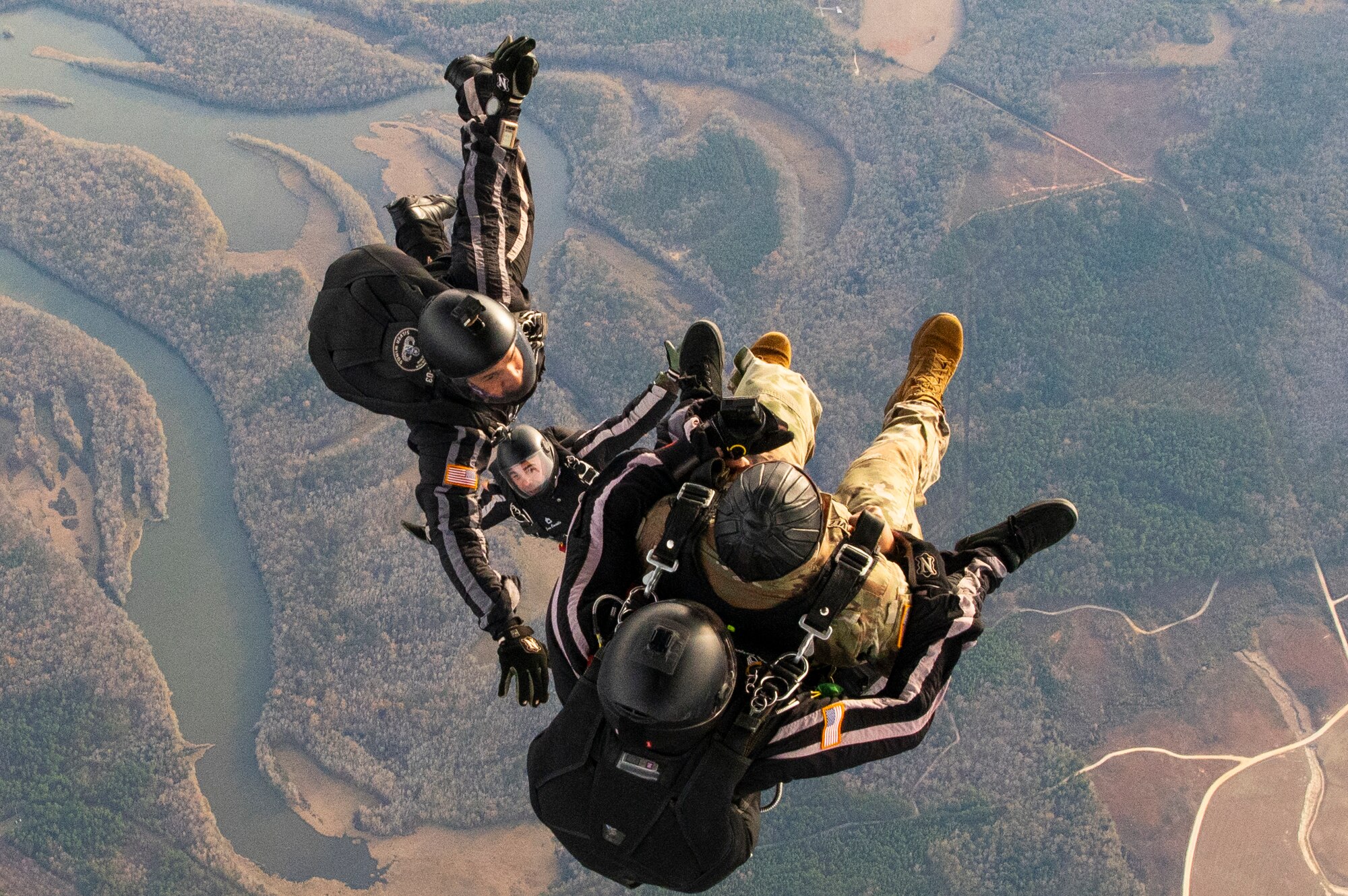 Three people free fall over the landscape after parachuting out of an aircraft