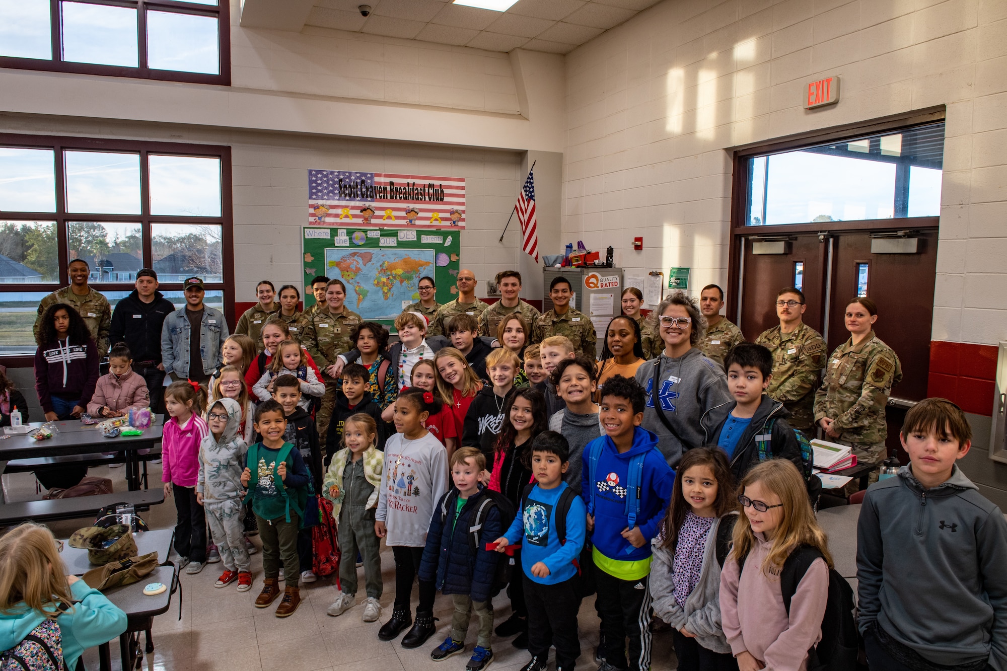 U.S. Air Force Airmen assigned to Moody Air Force Base,  smile with students at James L. Dewar Elementary School in Valdosta, Georgia, Dec. 15, 2023. The Airmen volunteered to serve breakfast to the Dewar Deployment Breakfast Club in an effort to support students who have a parent deployed during the holiday season. (U.S. Air Force photo by Courtney Sebastianelli)