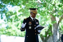 U.S. Army Chaplain (Lt. Col.) Jamison Bowman, Arlington National Cemetery Senior Army Chaplain, is standing in his dark blue Army dress uniform with white gloves. He has one hand holding a book and his other hand extended in a gesture as he gives remarks during modified military funeral honors for U.S. Army Sgt. 1st Class Frank Ehlinger in Section 60 of Arlington National Cemetery, Arlington, Virginia, July 23, 2020.