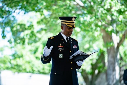 U.S. Army Chaplain (Lt. Col.) Jamison Bowman, Arlington National Cemetery Senior Army Chaplain, is standing in his dark blue Army dress uniform with white gloves. He has one hand holding a book and his other hand extended in a gesture as he gives remarks during modified military funeral honors for U.S. Army Sgt. 1st Class Frank Ehlinger in Section 60 of Arlington National Cemetery, Arlington, Virginia, July 23, 2020.