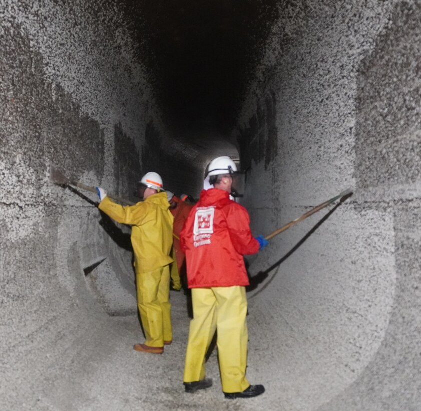 Photo of people in safety gear scraping barnacle buildup along filling tunnels.