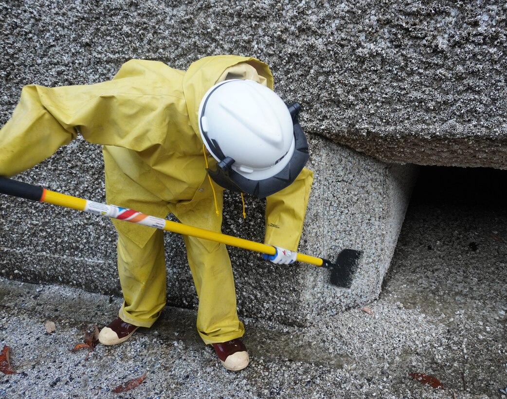 Photo of a person in safety gear scraping barnacle buildup along filling tunnels.