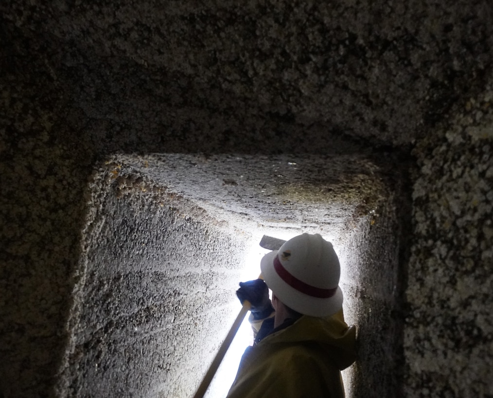 Photo of a person in safety gear scraping barnacle buildup along filling tunnels.